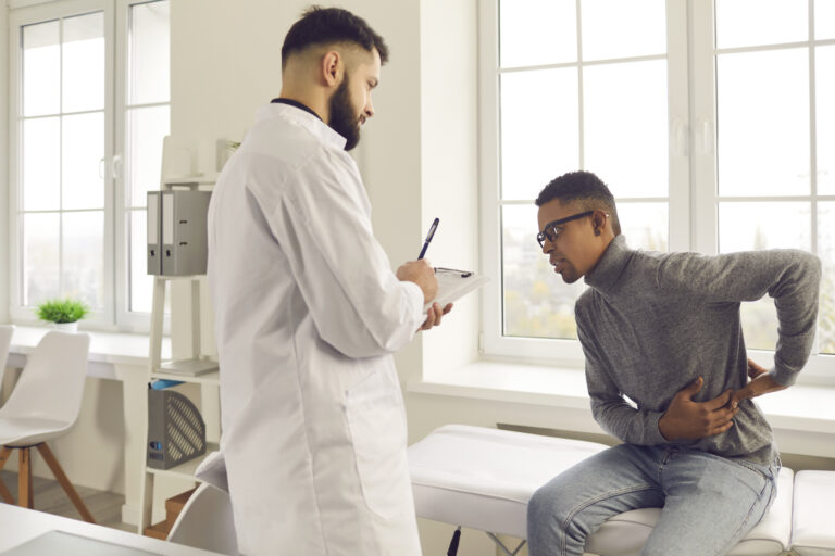 Pain management physician evaluating lower back pain in a patient during a clinical exam in Naples, Florida