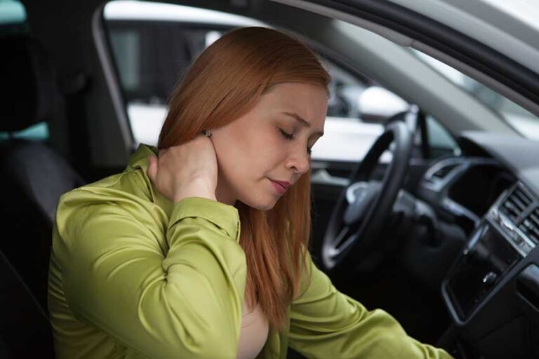 Woman sitting in her car holding her neck after a collision, representing whiplash symptoms after a car accident in Florida.