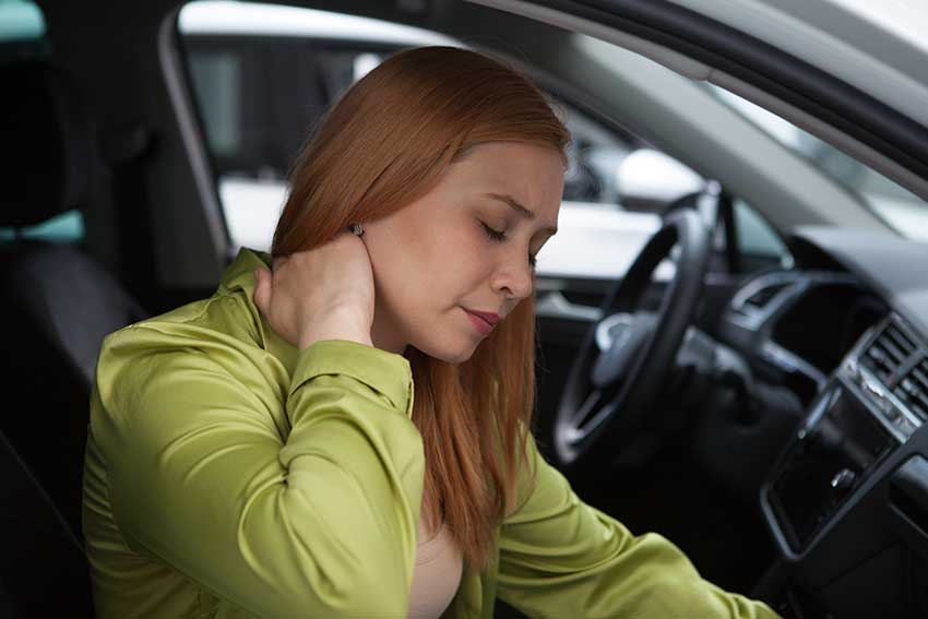 Woman sitting in her car holding her neck after a collision, representing whiplash symptoms after a car accident in Florida.