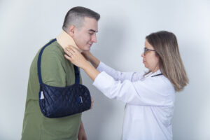 Healthcare provider checking a patient’s neck brace while the patient wears an arm sling during a post-accident injury evaluation.