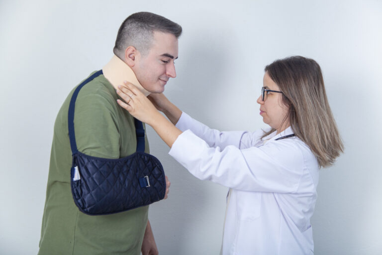 Healthcare provider checking a patient’s neck brace while the patient wears an arm sling during a post-accident injury evaluation.