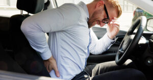 Man holding his lower back while sitting in a car, representing lower back pain after a car accident.