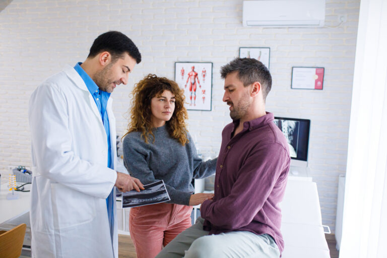Healthcare provider reviewing spinal imaging with patients during an evaluation for facet joint pain and medial branch blocks after a car accident.