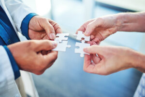 Hands holding puzzle pieces together, representing coordinated auto injury care and team-based rehabilitation.